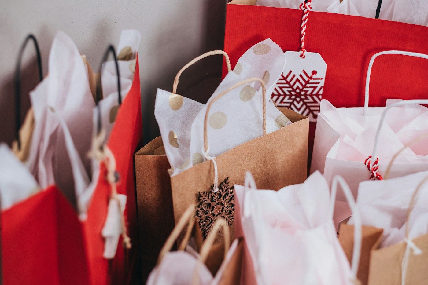 Red and kraft paper holiday shopping bags with tissue paper and gift tags, packed close together