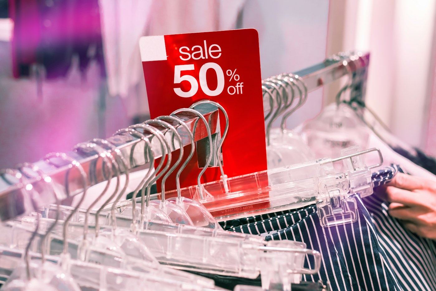 A red sale 50 percent off sign on a clothing rail, among clear plastic hangers